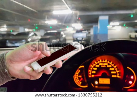 Man use mobile phone in the car, blur image of parking in the building as background.