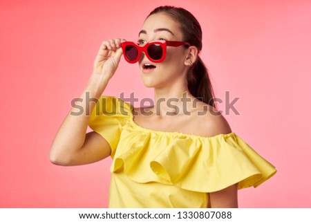  a woman in a yellow shirt lowered her glasses on a coral background                              