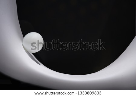 Ping pong ball is rolling along a white concave surface. Black background