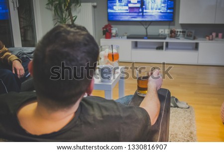 Unknown man relaxing, holding a glass with beer and watching television. View from the back.