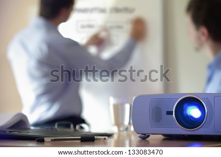 Business conference or lecture with businessman writing on whiteboard and lcd projector in foreground