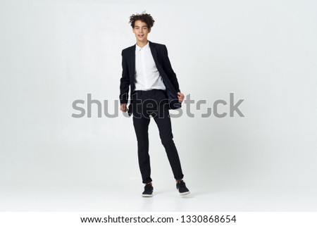 A man in black trousers classic shoes and a jacket on a gray background curly hair                        