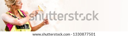 Female worker in coverall hold brush paint wall showing thumbs up finger gesture panoramic image copyspace for your advertisement text, construction industry, repair renovation and occupation concept 