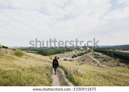 Young woman with a backpack walks through the rolling hills.