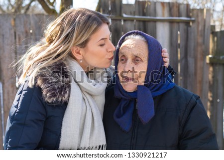 Picture of young beautiful woman kissing her old grandmother outdoor. Spending quality time together