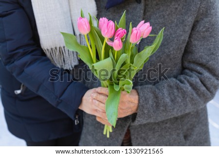 Close up picture of beautiful pink tulips - young woman giving a flower bouquet to her old grandmother