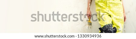 Female builder worker legs cropped image wearing yellow protective coverall holding paint brush standing over obsolete old panoramic blank background for text advertisement, repair renovation concept