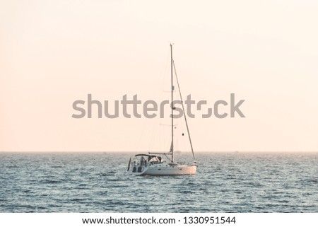 Little white boat floating on the water towards the horizon in the rays of the setting sun