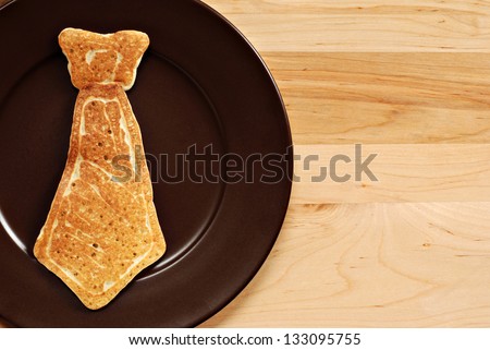 Father's day background image with real pancake in the shape of a necktie on plate.  Closeup with wood background and copy space. Royalty-Free Stock Photo #133095755