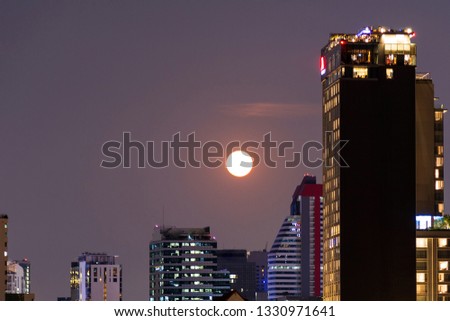 Cityscape picture with business district with high building at night with big moon in the sky.