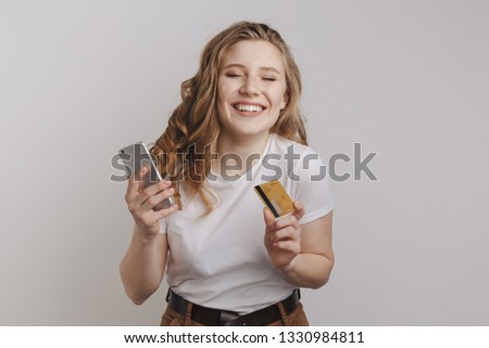 Happy curly hair young woman posing with phone and credit card isolated over the white background.
