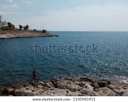 Fisherman on the rocky coast of sea in the sunny day