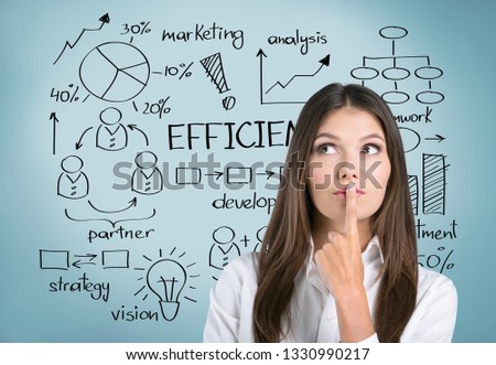 Pensive young businesswoman wearing a suit is holding a pen and thinking. A gray wall background with an infographic on it