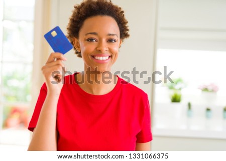 Young african american woman holding credit card with a happy face standing and smiling with a confident smile showing teeth