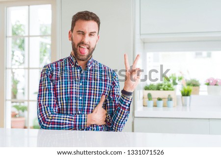 Handsome man wearing colorful shirt smiling with happy face winking at the camera doing victory sign. Number two.