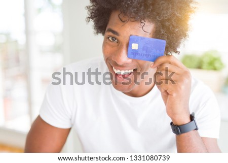 African American man holding credit card with a happy face standing and smiling with a confident smile showing teeth