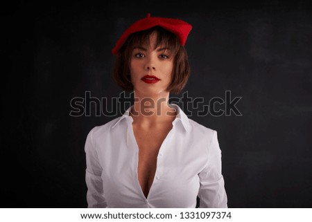 Portrait shot of young woman wearing wool beret and white shirt while standing at dark background. 