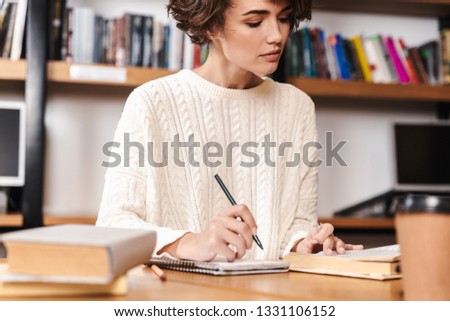 Smiling young student girl studying while sitting at the library desk