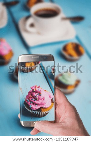 Man taking photo of Chocolate cupcake with colored pink and green cream on blue table
