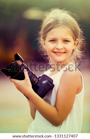 smiling girl  8-10 years old in elementary school age holding photo camera in hands outdoors