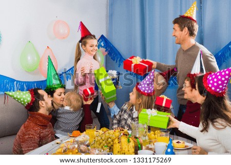 Large positive smiling family presenting gifts to girl during birthday party