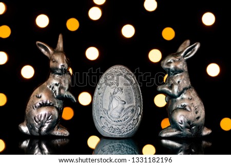 Two silver easter bunnies and a white easter egg with reflection and beautiful bukeh in front of a black background