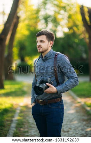 Portrait of handome photographer outside. Man use strap for professional camera. Expensive lens