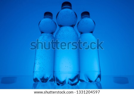 toned image of plastic water bottles in row on neon blue background