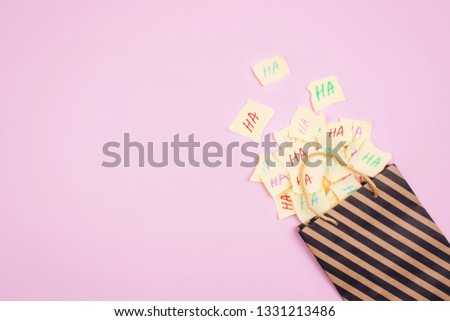 April Fools' Day celebration background. Paper bag with many paper sheets with the words haha. 1 April mockup on pink background. All Fools' Day, humor, prank, joke concept