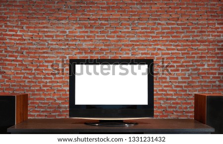 LCD television cuts out white screen on wooden table in living room with brick wall background.