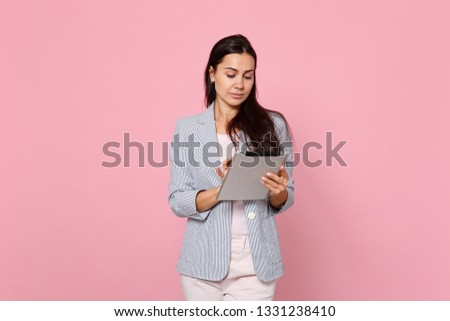 Portrait of beautiful pretty young woman in striped jacket using tablet pc computer isolated on pink pastel wall background in studio. People sincere emotions, lifestyle concept. Mock up copy space