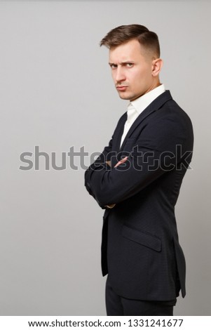 Side view of displeased young business man in classic black suit, shirt holding hands folded isolated on grey wall background in studio. Achievement career wealth business concept. Mock up copy space