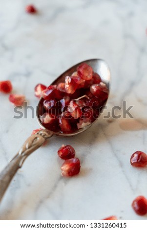 Ripe pomegranate seeds on marble background with antique spoon. White and light photography. 