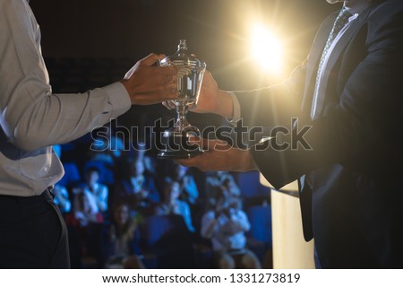Side view of Caucasian businessman giving trophy to mixed race business male executive on stage in auditorium Royalty-Free Stock Photo #1331273819