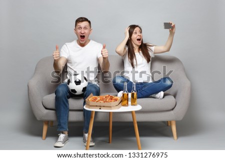 Excited couple woman man football fans cheer up support favorite team, expressive gesticulating hands show thumb up doing selfie shot on mobile phone isolated on grey background. Sport family concept