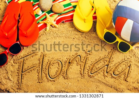 Summer concept of sandy beach, colorful thongs shoes, sunglasses, ball and inscription florida