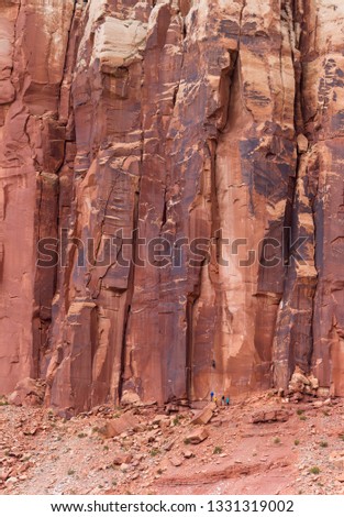 Large red rock butte in characteristic of the American southwest with a group of unrecognizable people climbing the red rock face