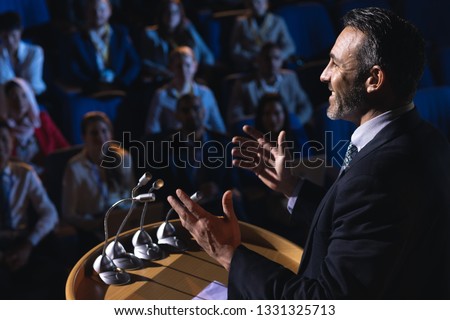 Side view of Caucasian businessman standing and giving presentation in the auditorium  Royalty-Free Stock Photo #1331325713