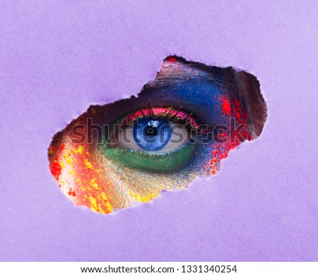 Cosmetics sale. Eye of young woman with bright artistic makeup looking through paper hole