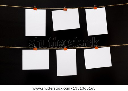 empty paper cards attached with colorful clothespins on linen rope on a black background, blank templates for images or text, concept office and photo industry, decor