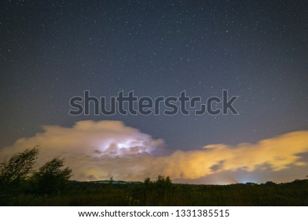 Powerful thunderstorm with lightnings at night with starry sky on the background.