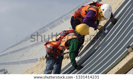 construction workers wearing harness helmet sunglass and sun mask in construction site to  metal sheet installtion roofing Royalty-Free Stock Photo #1331414231