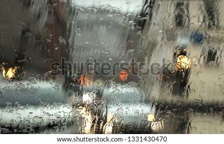 Automobile road glass and water drops close up. Rain outside the window in the sity blurred silhouettes. Traffic jam. 