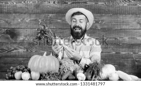 Farmer with homegrown harvest. Farmer rustic villager appearance. Man cheerful bearded farmer hold horseradish wooden background. Grow organic crops. Farmer straw hat presenting fresh vegetables.