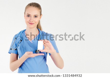 Girl doctor blond gray background beautiful smiling positive light hand holding medication bottle. Concept of good tools patient. Index finger raised.