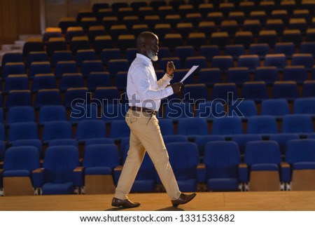 Side view of old African-American businessman practicing and learning script while walking in the auditorium Royalty-Free Stock Photo #1331533682