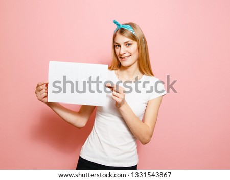 A beautiful blond girl laughing with a white billboard in her hand on a pink background