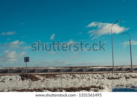 View of blue sky and road and road signs with lanterns, bright Sunny winter day. Empty asphalt road, turns, snow, white drifts and clouds floating on the blue sky