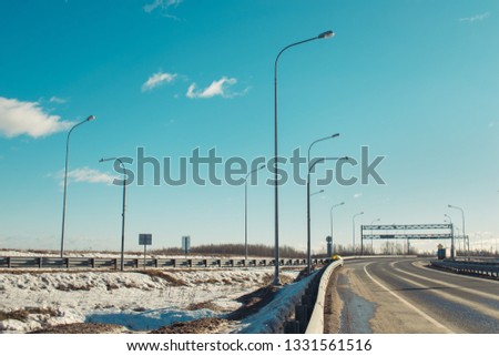 View of blue sky and road and road signs with lanterns, bright Sunny winter day. Empty asphalt road, turns, snow, white drifts and clouds floating on the blue sky