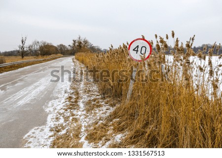 Winter road covered with snow with old speed limit traffic sign